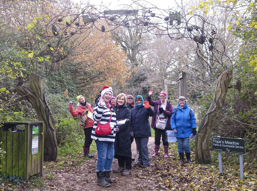 Photo of members enjoying a geocaching session, most waving at camera. Entering Pope's Meadow.